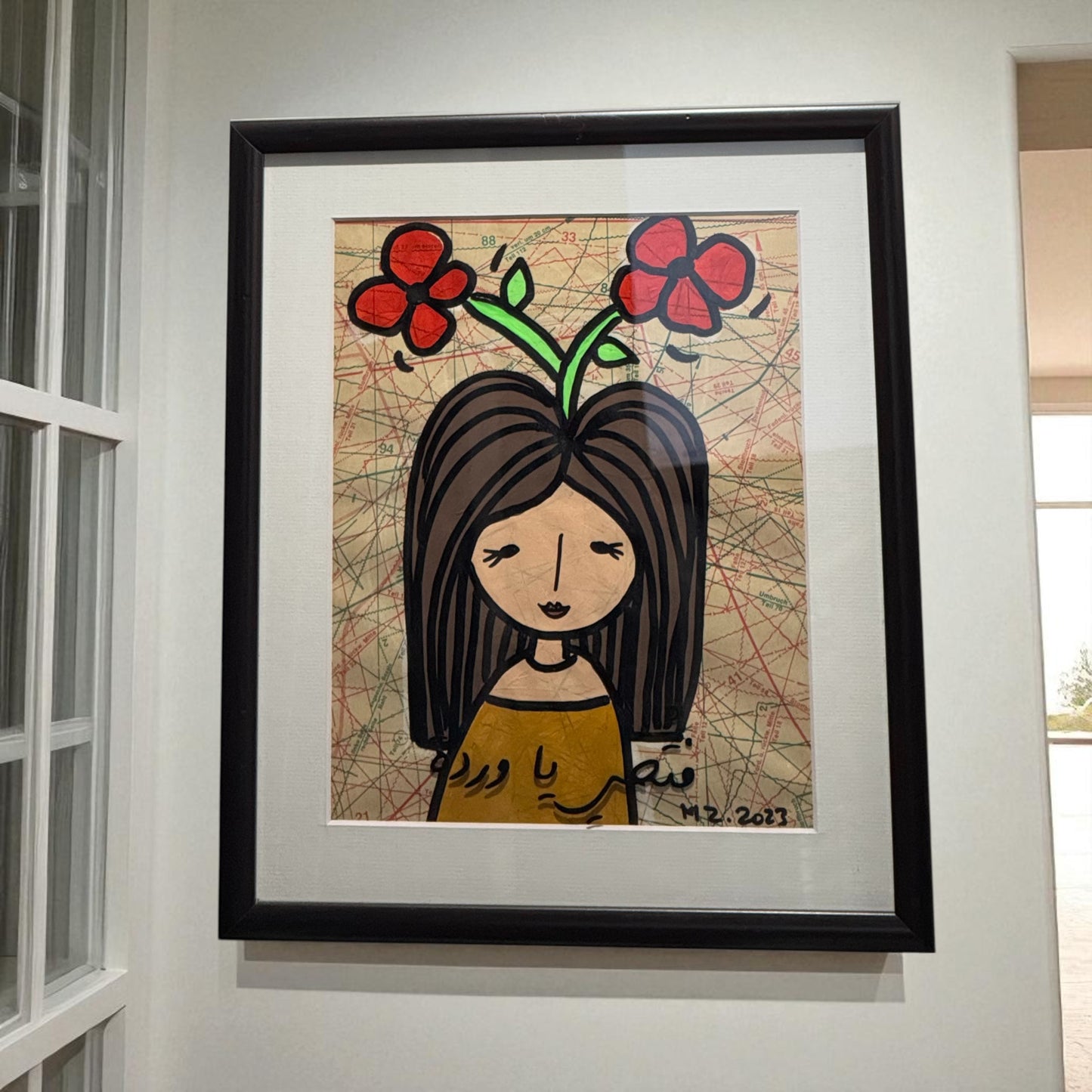Framed artwork of a woman with flowers on her head, displayed on a wall.